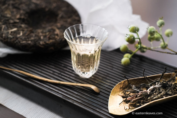 Glass cup with Chinese pu'er tea from Yunnan, in loose-leaf and pressed brick or cake, with copper tools and teaware and green berries